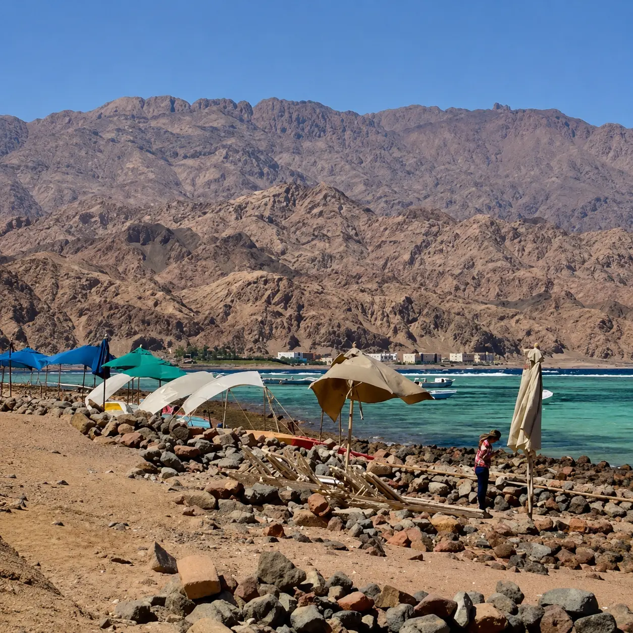 شاطئ دهب بمظلاته الملونة ومياهه الفيروزية وجبال سيناء في الخلفية